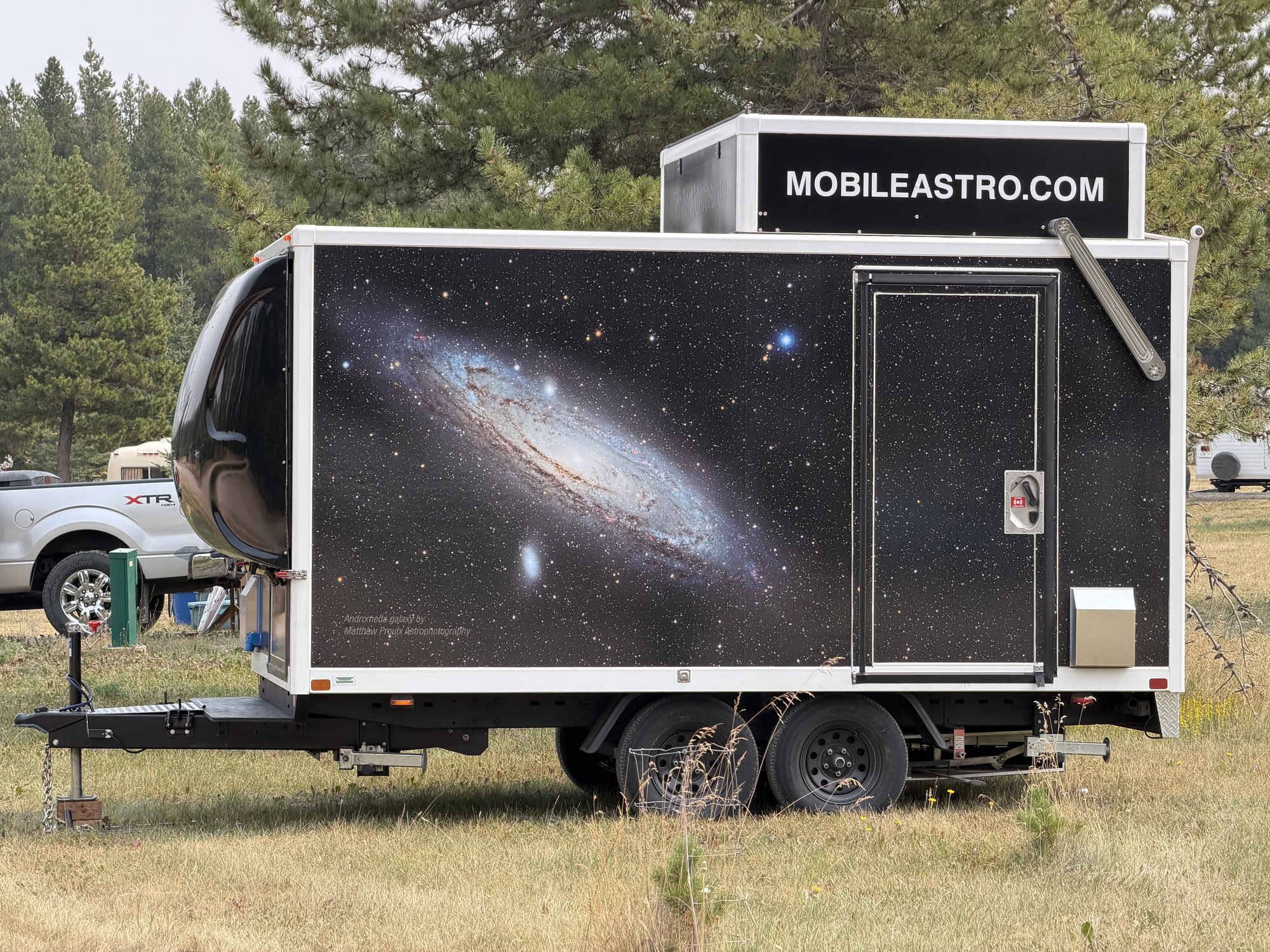 The Mobile Astro trailer parked and sealed among pine trees, roof closed